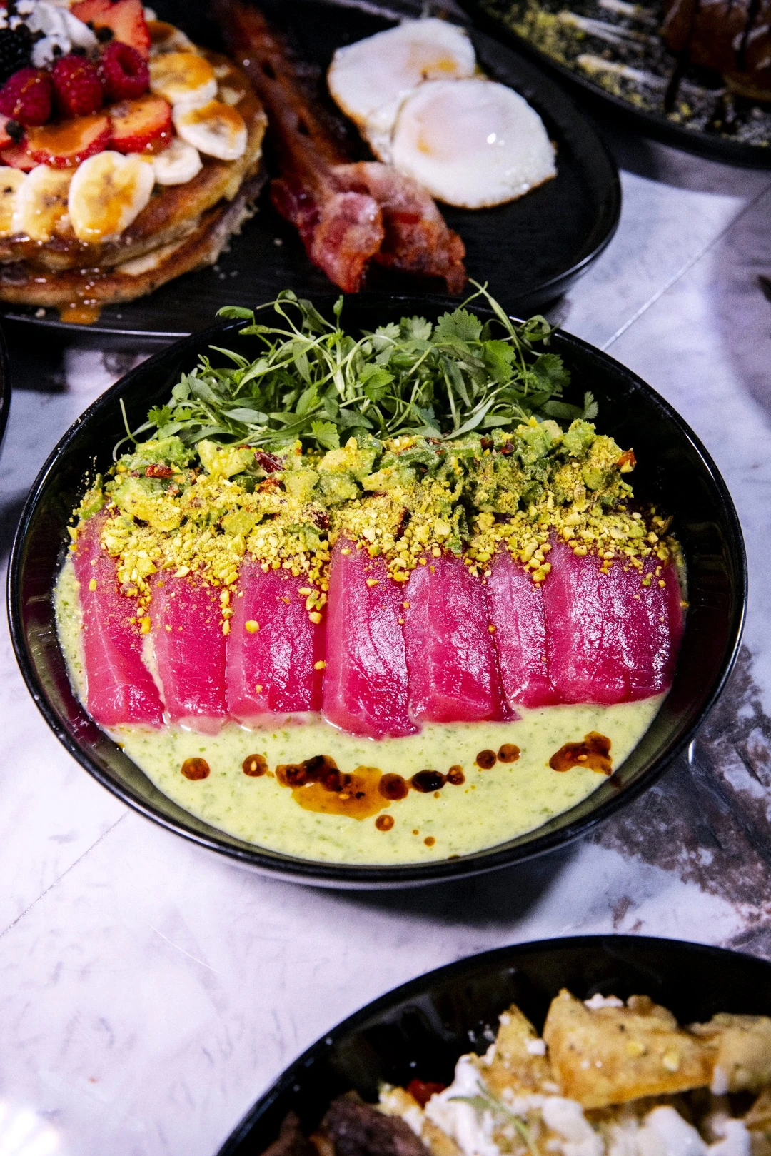 Sliced tuna with greens and sauce on a complete black plate at Mousai.