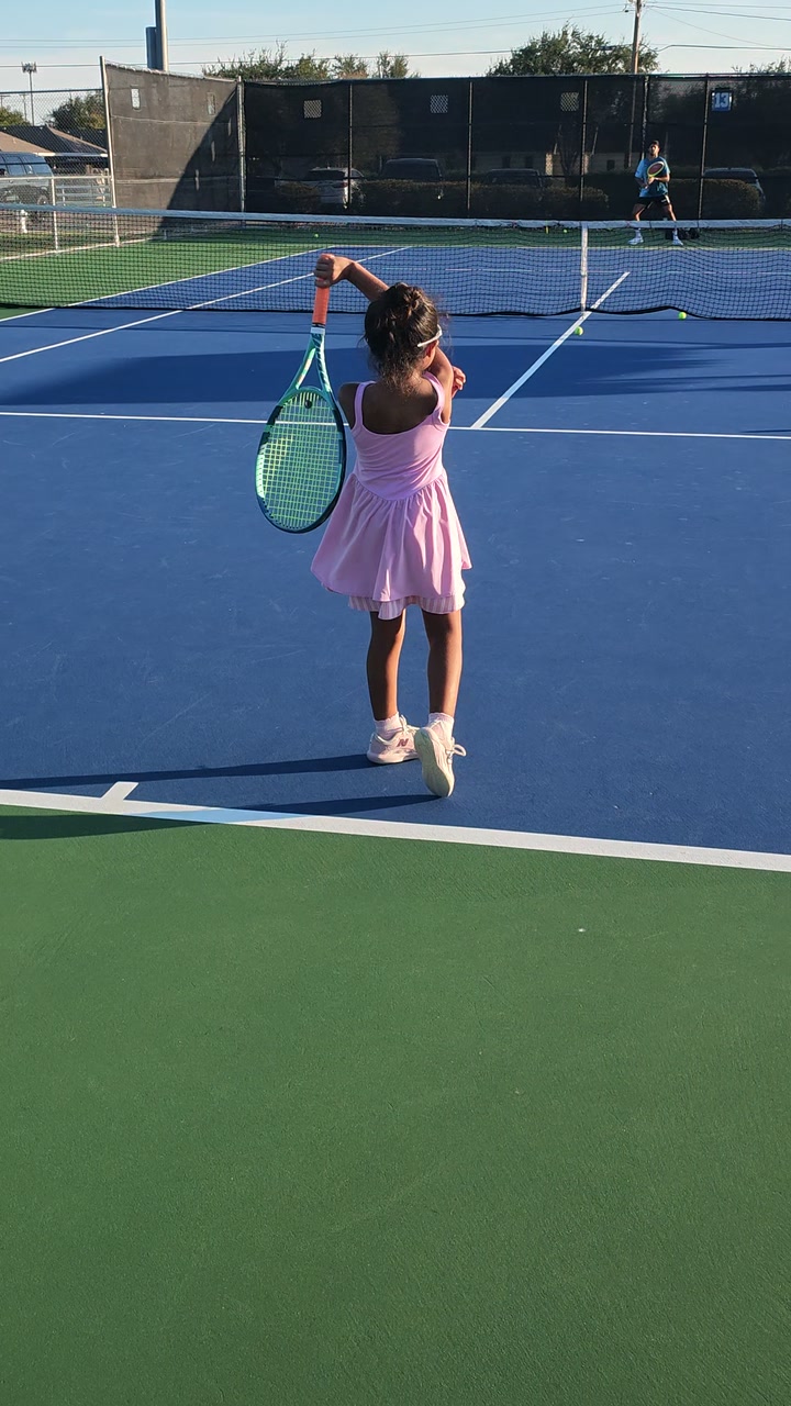 Penny preparing to serve, seen from the rear of the tennis court